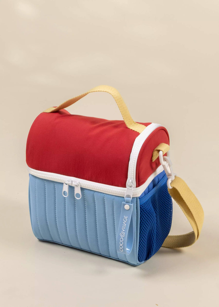 Two-toned red and blue cooler bag with a yellow strap on a beige background