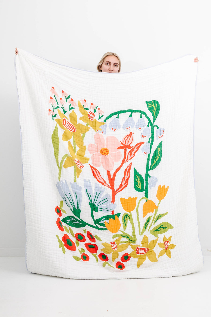 Person holding a large decorative pillow with floral design on a white background