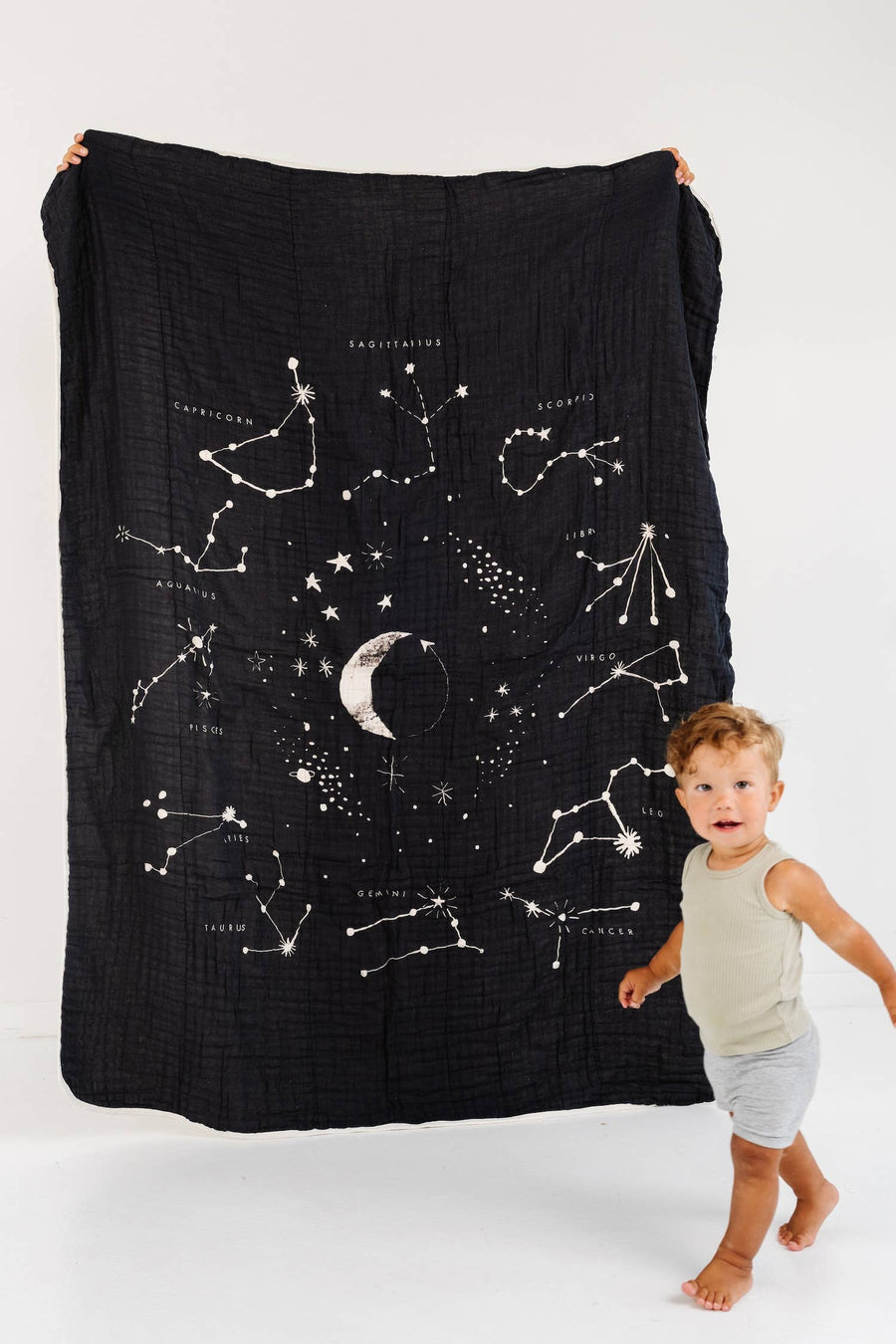 Child holding a black blanket with star constellations on a white background